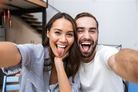 Premium Photo Cheerful Multiethnic Couple Taking A Selfie While Sitting At The Kitchen