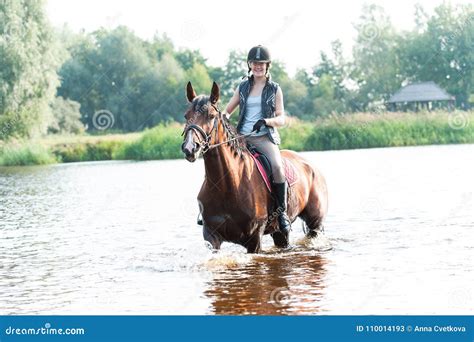 Cheerful Young Teenage Girl Riding Horseback In River At Morning Stock