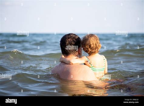 papa hält ein kleines süßes kleinkind tochter im meerwasser und beobachten den horizont zurück