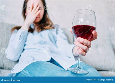 A Woman Is Sitting On A Sofa Holding Her Hand On Her Face And Holding A Glass Of Wine Stock