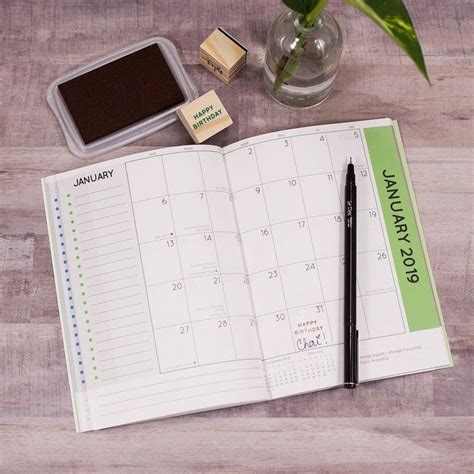 An Open Planner With Stamps And A Pen On A Wooden Table Next To A