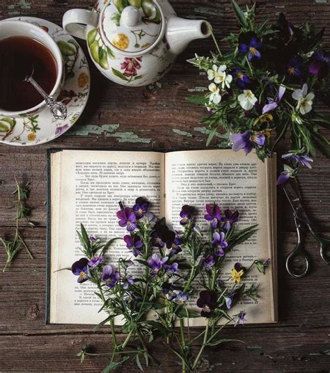An Open Book Sitting On Top Of A Wooden Table Next To Flowers And Tea Cups