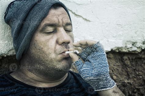 A Homeless Man With Gloves And A Dirty Face Is Smoking A Cigarette