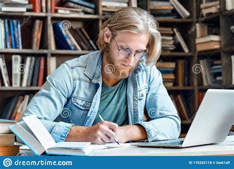 Young Concentrated Male Student At Library Desk Modern Laptop Write In
