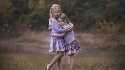 Cute Little Girls Are Hugging Each Other In Blur Trees