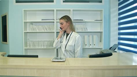 Female Nurse At Hospital Reception Answering Phone Calls And Scheduling