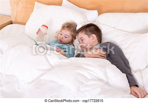 Happy Little Brother And Sister Lying In Bed Together As They Cuddle