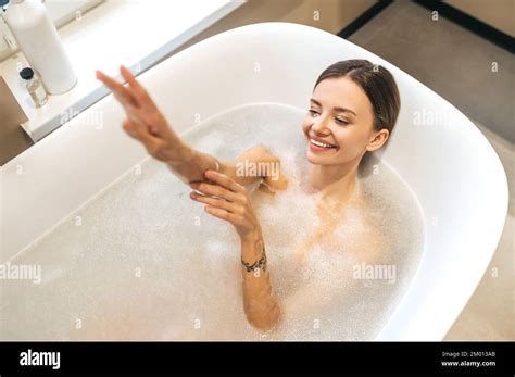 Top View Of A Smiling Beautiful Woman Lying In The Bathtub Filled With Soapy Water Stock Photo