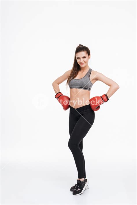Full Length Portrait Of A Satisfied Smiling Fitness Woman Wearing Boxing Gloves And Standing