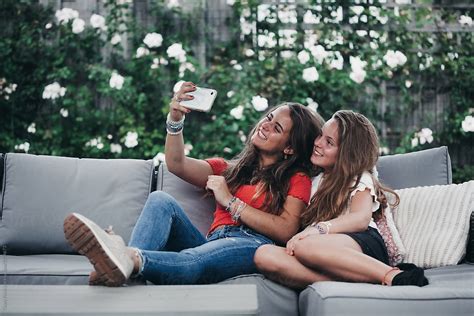 Sisters Sitting On The Couch In The Garden Taking A Selfie By Stocksy