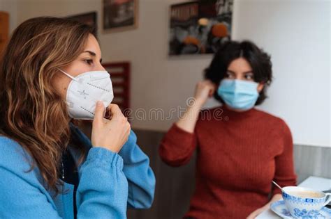 Two Women Wearing Medical Masks Sitting In The Cafe Drinking Coffee