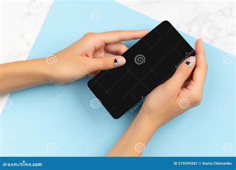 Female Hand Holding Mobile Phone On Marble And Blue Background Stock