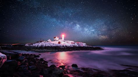Snow Covered Hill With Lighthouse Under Blue And Black Sky With Stars