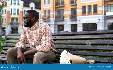 Sad African Man Sitting Lonely On City Bench With Flower Bouquet
