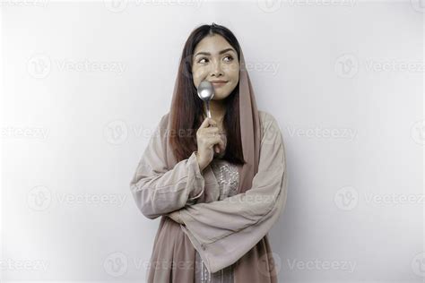 ett asiatisk muslim kvinna är fasta och hungrig och innehav bestick medan ser åt sidan tänkande