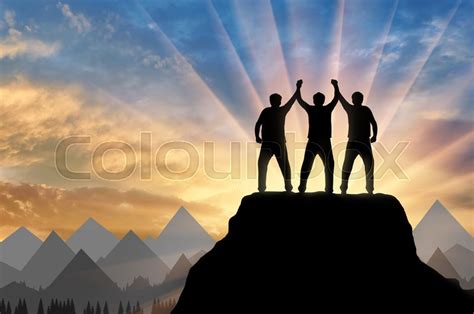 Silhouette Of Happy Three Climbers On The Top Of The Mountain Holding