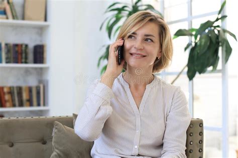 Pretty Blond Middle Aged Woman Talking On Mobile Phone Sitting On Sofa