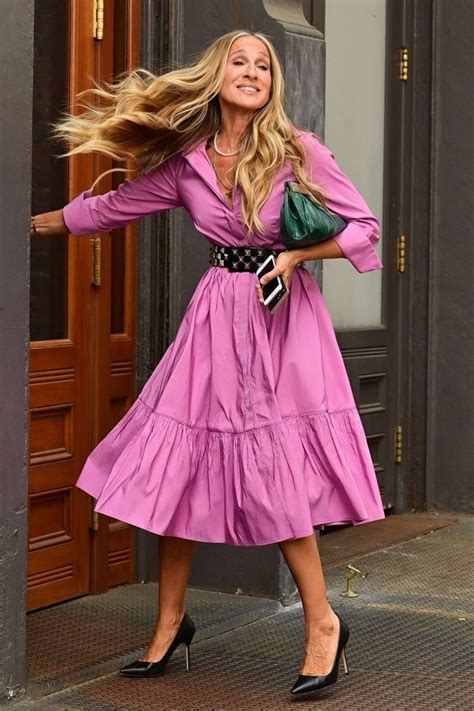 a woman in a pink dress is walking down the street with her hair blowing in the wind