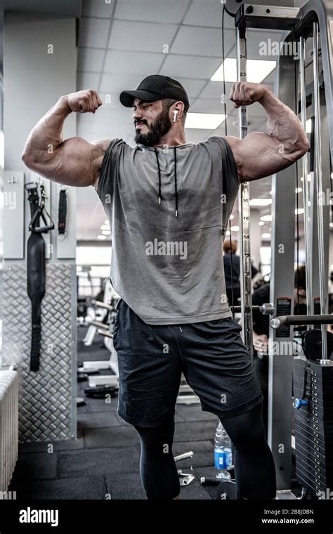 Handsome Strong Male With Beard Wearing Sportswear And Cap Showing Double Biceps Muscular Pose