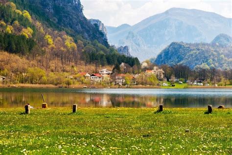 A Lake With Mountains In The Background And Grass On The Ground Next To It