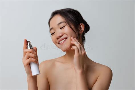 Portrait Of Young Beautiful Woman Taking Care After Skin Using Moisturizing Cream Over Gray