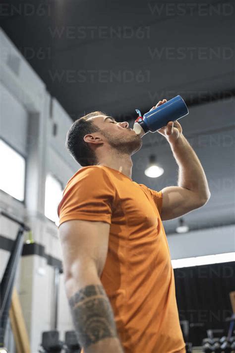 Thirsty Man Drinking Water While Standing In Gym Stock Photo