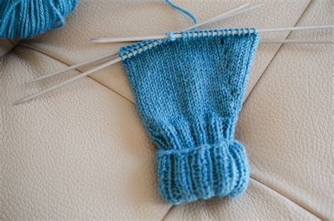 A Blue Knitted Mitt Sitting On Top Of A White Couch Next To Knitting