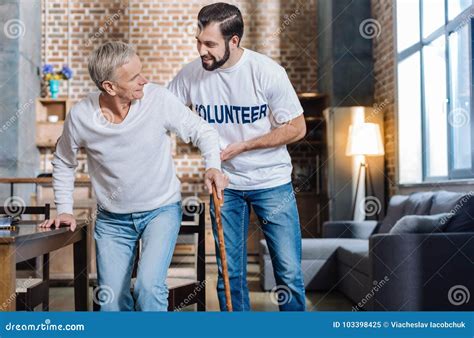Pleasant Kind Volunteer Supporting A Senior Man And Helping Him While