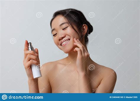 Portrait Of Young Beautiful Woman Taking Care After Skin Using Moisturizing Cream Over Gray