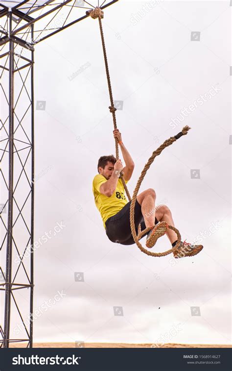 Young Man Climbing A Rope Of Knots In A Spartan Race Extreme Sport