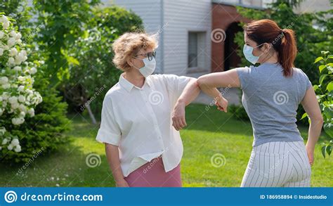 Two Masked Women Greet Their Elbows In The Park An Elderly Woman And Her Daughter Maintain