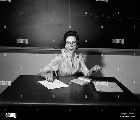 1950 profesora de escuela con gafas sentado en una mesa en el aula mirando a la cámara