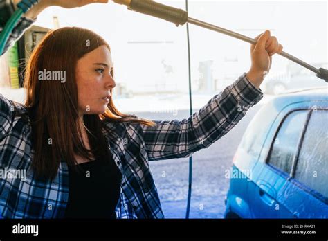 Medium Shot Of A Young Woman Washing Her Car In A Public Car Wash Stock