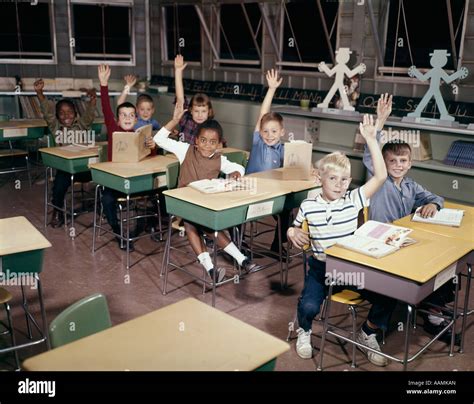 1960s Elementary School Children In Classroom With Hands Raised To