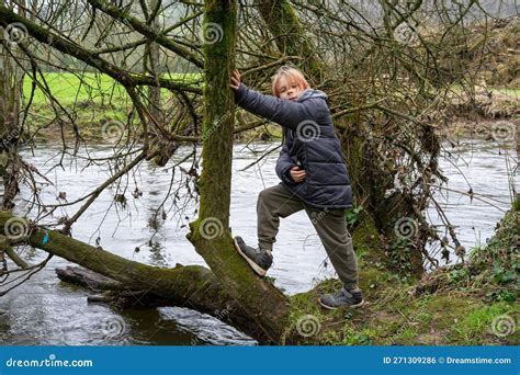 A Young Boy On A Fallen Tree Near The River A Boy With Long Hair In A