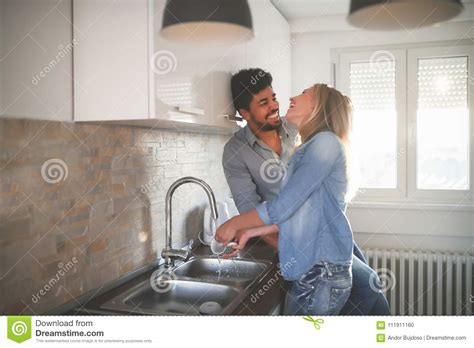 Young Couple Doing Dishes In The Kitchen And Smiling Stock Photo