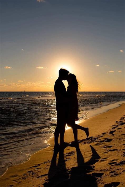 Two People Kissing On The Beach With The Sun Setting In The Backgrounnd