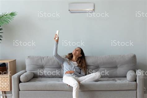 Smiling Woman Relaxing On Couch Using Air Conditioner Remote Controller