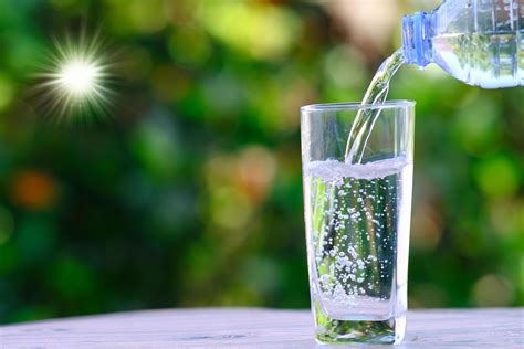 Hand Pouring Water Into A Glass Cup With A Bokeh Nature Background