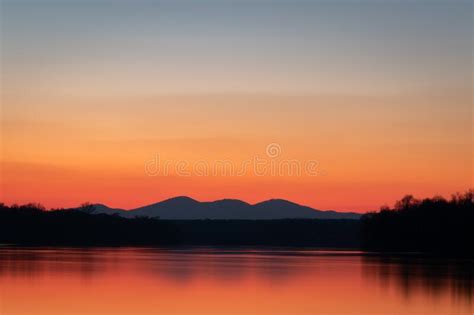 River And Mountain Silhouette With Red Glow At Horizon During Twilight