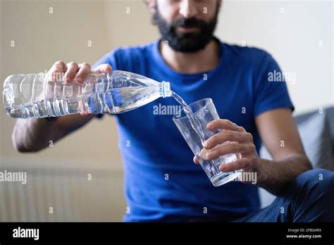 Thirsty Young Man Pouring Water In Drinking Glass At Home Stock Photo
