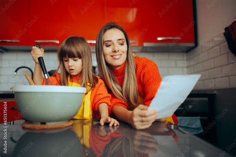 Mother Checking A Recipe While Cooking Next To Her Daughter Mom And Daughter Making Traditional