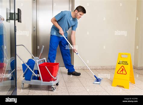 Happy Male Janitor With Cleaning Equipments Mopping Floor Stock Photo