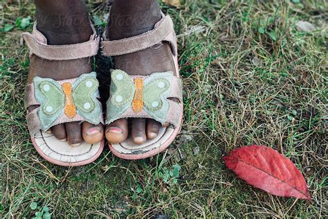 fallen red leaf next to a black girl s feet wearing sandals by stocksy contributor gabi