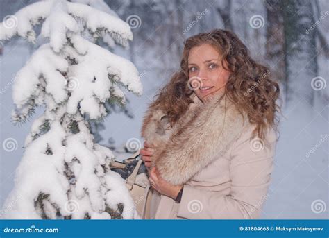 Winter Portrait Of A Woman In White Coat During Snowfall In A Park