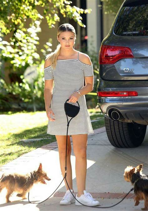 A Woman In A Striped Dress Is Walking Her Dog On A Leash And Looking At