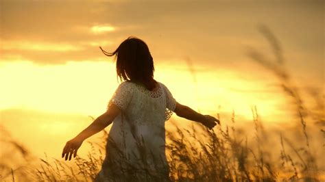 Beautiful girl wearing white dress running through beautiful field at sunset. Young woman ...