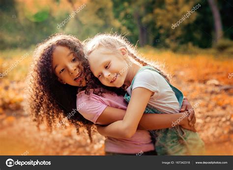 Две счастливые девушки как друзья обнимают друг друга весело Маленькие подружки в парке