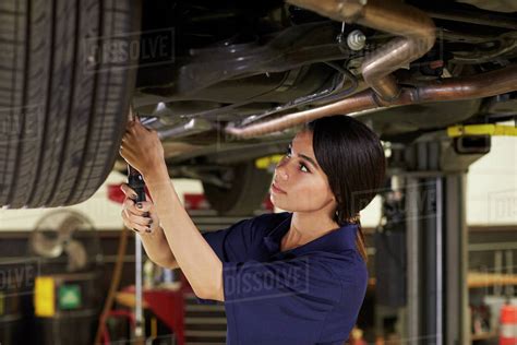Female Auto Mechanic Working Underneath Car In Garage Stock Photo