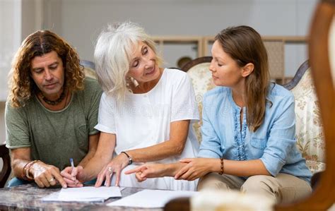 Mature Mother And Adult Children Fill Out Paperwork In Room Stock Photo